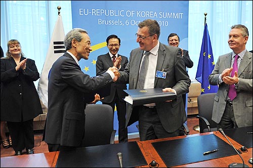 2010년 벨기엘 브뤼셀에서 한-EU FTA 공식 체결 서명 후 각 대표가 악수하는 모습을 이명박 대통령이 뒤에서 웃으며 바라보고 있다. 