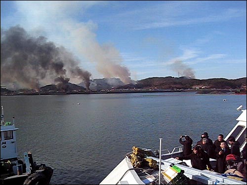 연평도 부두에서 여객선을 타고 있는 승객들이 포탄이 폭발하면서 섬 곳곳에서 피어오르는 시커먼 연기를 지켜보거나 촬영하고 있다. 연평도를 방문한 한 시민이 제공한 화면.