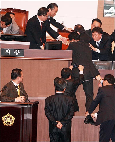 의장석에서 끌려나오며 바지가 찢어진 한 한나라당 의원이 다시 올라가려하자 민주당 의원들이 옷과 다리를 잡아 끌어내리고 있다.