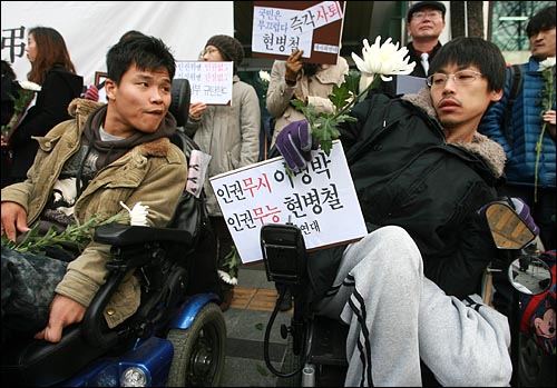 한 중증장애인이 '인권무시 이명박, 인권무능 현병철'이 적힌 피켓을 휠체어에 붙이고 있다.