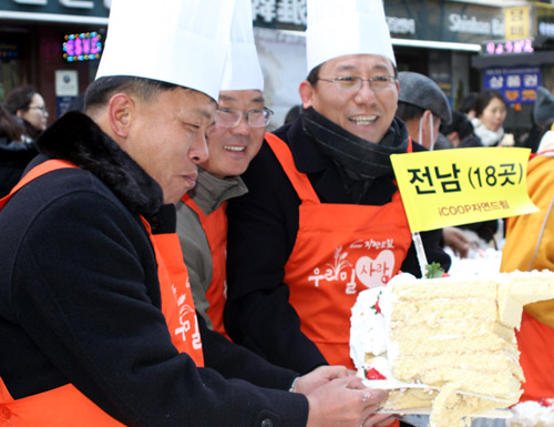 iCOOP생협이 15일 서울 명동 우리은행 앞에서 크리스마스를 앞두고 유기농 우리밀로 만든 대형 케이크를 제작, 시민들에게 시식행사를 진행했다. 행사에 참석한 생산자들이 우리밀 케이크를 잘라 들어 보이고 있다.