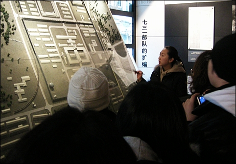 731부대 조감도 앞에서 세균폭탄 제조실, 독가스 제조실, 동상 실험실 등이 있었던 곳을 지적하며 설명하는 여성 해설사와 방문객들. 
