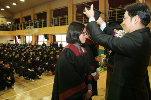 상정중에 졸업가운과 사각모를 기증한 선린교회의 권구현 담임목사가 졸업생 대표에게 가운을 입히고 있다. 