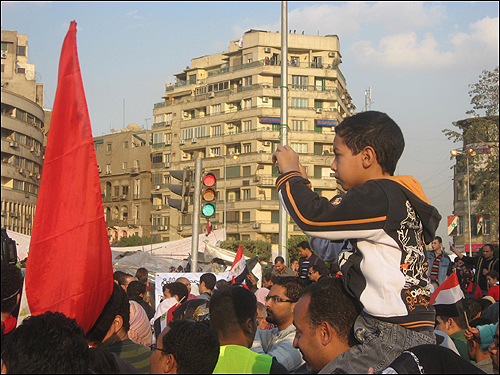 12일(현지 시각) 이집트 수도 카이로의 타흐리르 광장에 수많은 시민이 모여 '무바라크 사임'을 이끌어낸 것을 자축하고 있는 가운데, 목말을 탄 한 어린이가 디지털카메라로 현장을 촬영하고 있다.
