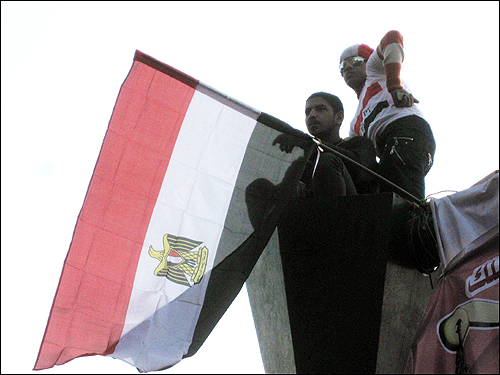 12일(현지 시각) 이집트 수도 카이로의 타흐리르 광장에 수많은 시민이 모여 '무바라크 사임'을 이끌어낸 것을 자축하고 있는 가운데, 두 사람이 국기를 들고 높은 가로등 위에 올라가 있다.