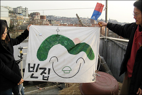 서울 해방촌에 있는 '빈마을'의 '아랫집' 옥상에서 김수진 인턴기자와 장기투숙객 지음이 빈집 깃발을 펼쳐보이고 있다.