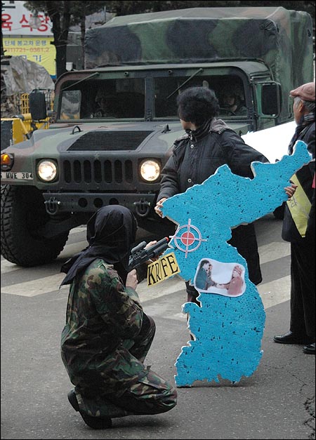 2011년 키리졸브/독수리연습이 시작된 2월 28일, 경기도 성남시 청계산 자락의 한미연합사 전쟁지휘소(TANGO) 앞에서 열린 반전평화단체의 집회 상징의식이 진행되는 가운데 훈련에 참가한 미군 차량이 지나가고 있다. 