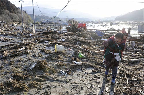 지난 2011년 3월 12일 진도 8.8의 초강력 지진이 발생한 일본의 동북부 해안과 인접한 이와테현에서 12일 오전 어린 아이를 업은 한 여성이 쓰나미로 인해 잔해와 진흙으로 가득찬 곳을 지나고 있다.