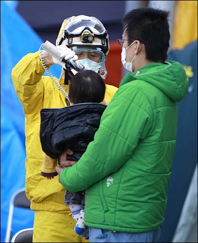 13일 일본 후쿠시마현 고리야마시에서 제1원자력발전소 폭발현장 인근서 대피한 한 남성이 자신의 아이가 방사선 노출 여부 검사를 받는 모습을 지켜보고 있다.