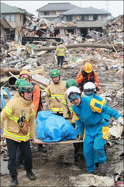 일본 동북지방에 진도 9의 강진이 발생한지 나흘이 지난 2011년 3월 15일 오전 119중앙구조단원들이 지진으로 인한 쓰나미 피해지역인 일본 미야기현 센다이시 미야기노구 가모지구에서 센다이 경찰과 함께 실종자 시신을 옮기고 있다.