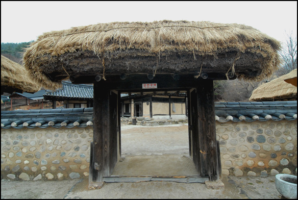 초가로 된 사주문 안으로 안채가 보인다. 충북 청원군 문의면 문의문화재단지 안에 소재한다