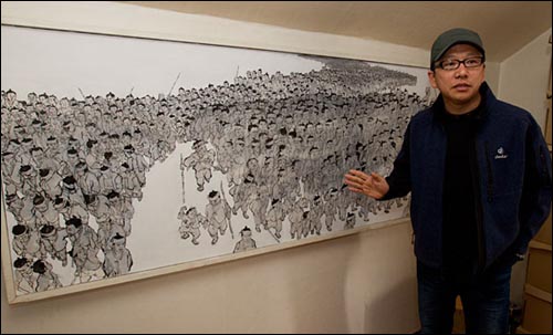 김규항이 그의 작업실에 있는 그림 '강'에 대한 설명을 하고 있다. '강'은 최호철 작가의 작품으로 동학농민군들이 강처럼 대열을 이루어 진군하는 모습을 그린 작품이다.