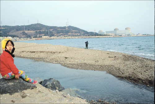 멀리 고리 원전이 보이는 바닷가에 한 어린이가 앉아 있다.