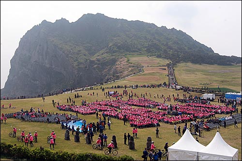  24일 오전 서귀포시 성산 일출봉 잔디광장에서 '제주-세계 7대 자연경관 선정 범국민추진위원회' 주최로 열린 '세계 7대 자연경관 제주 선정기원 관광문화축제'에서 제주도민들이 제주도가 선정되길 염원하며 분홍색 티셔츠를 입고 의자에 앉아 'N7W JEJU' 글자를 연출하고 있다.