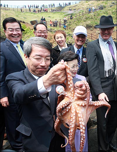 '세계 7대 자연경관 제주 선정기원 관광문화축제'에서 정운찬 범국민추진위원장이 해녀로부터 건네받은 문어를 들어보이자, 이참 한국관광공사 사장과 이배용 국가브랜드위원장, 뉴세븐원더스 설립자 버나드 웨버, 우근민 제주도지사가 이를 지켜보며 환하게 웃고 있다. 