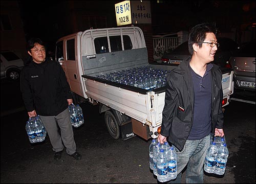'물 공급 원정대'를 주도한 김성주(오른쪽)씨와 박대용 춘천MBC 기자가 12일 새벽 경북 구미시 오태동 단수 지역인 대동 1차 아파트를 찾아와 주민들에게 전달하기 위해 차에서 생수를 옮기고 있다.