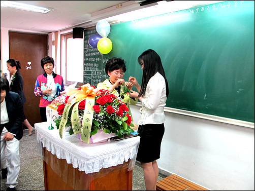 재학생 대표가 담임 강래경 선생님께 꽃다발과 카네이션을 가슴에 달아 드리고 있다. 