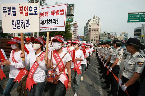 여경들이 폴리스라인을 들고 있는 가운데, 성매매 업소 단속에 항의하는 성매매 여성들이 춘천시내 거리행진을 벌이고 있다.