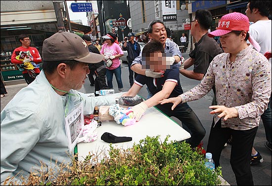  구청 단속반과 용역업체 직원들이 강제로 물건을 빼앗자, 노점상 주인들이 이를 저지하고 있다.
 