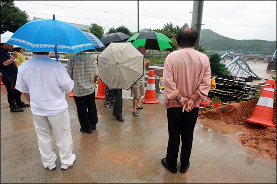 많은 칠곡 주민들이 우산을 쓰고 나와 무너진 호국의 다리를 바라보고 있다.