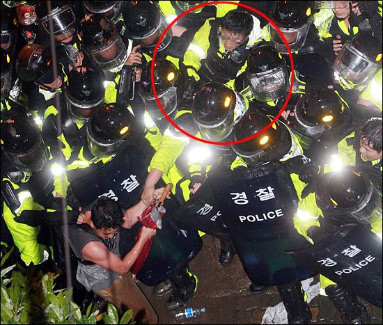 경찰 여러명이 한 집회 참가자의 목덜미와 팔을 잡고 꼼짝못하게 한 뒤, 얼굴을 향해 최루액(캡사이신 성분)을 조준 발사하고 있다.