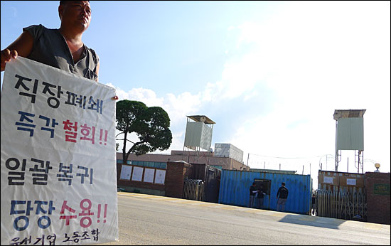 금속노조 유성기업지회 조합원이 7월 18일 오후 충남 아산시 둔포면 운용리 유성기업의 굳게 잠긴 정문 앞에서 '사측은 직장폐쇄를 풀고, 조합원들의 일괄복귀를 허용하라'는 내용의 팻말을 들고 1인 시위를 벌이고 있다.