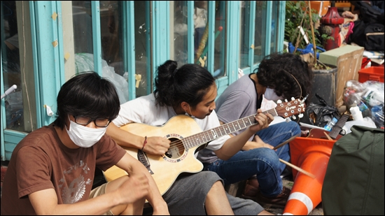 학생들이 카페마리에서 쫓겨나 도로 위에서 기타를 치며 노래하고 있다.