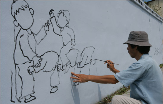 이재관 씨가 전라남도 곡성군 목사동면 평리마을 담벼락에 벽화 밑그림으로 말뚝박기 놀이 그림을 그리고 있다.