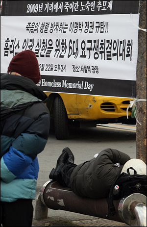2009년 12월 22일 서울역 광장에서 열린 거리에서 죽어간 노숙인 추모제 행사장의 현수막 밑 벤치에 노숙인이 잠들어 있다. 