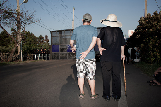 강정마을 도로를 봉쇄한 경찰 바리케이드 앞에 서있는 여균동 감독과 문규현 신부. 