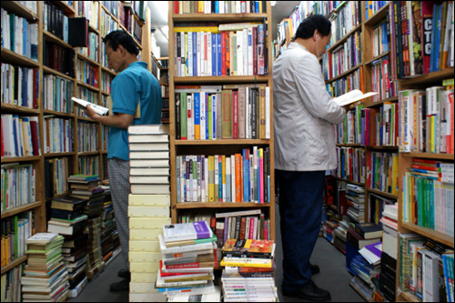 좁은 공간 빼곡히 쌓인 책 사이로 사람들이 책을 고르고 있다.