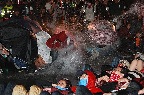 29일 오후 서울 중구 을지로입구역 사거리에서 경찰들이 반값등록금 실현을 촉구하며 도로 점거시위를 벌이는 학생들에게 물대포(살수차)를 발사하자, 학생들이 우산을 이용해 맞서고 있다.