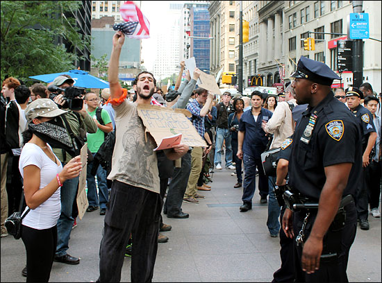 타락한 금융자본주의와 경제적 불평등에 항의하면서 시작된 미국 뉴욕 월스트리트 점거 시위가 장기화 양상을 보이고 있다. 점거 시위 첫날 수백명에 불과했던 시위대는 14일이 지난 9월 30일(현지 시각) 2000여명으로 급격히 불어났다. 이들은 이날 뉴욕시 경찰청을 향해 항의 가두행진을 벌였다. 사진은 뉴욕 로어 맨해튼 브로드웨이와 리버티 스트리트 코너에 위치한 자유광장(주코티 파크) 앞에서 한 시위대가 인도에서 시민들을 향해 구호를 외치자, 경찰이 광장 안쪽으로 들어가라고 제지하는 모습. 

