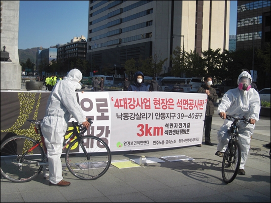 25일 서울 광화문 광장에서 환경보건시민센터 회원들이 방진복 차림에 방독면을 쓰고 4대강 자전거 길을 달리는 퍼포먼스를 하고 있다. 
