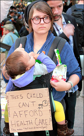 '월스트리트 점령' 시위가 벌어지고 있는 뉴욕 맨해튼 자유광장(주코티파크) 앞에서 한 아이의 어머니가 '(복지 예산 축소로) 아이의 의료비를 감당할 여력이 없다'는 내용의 손팻말을 들고 서 있다.