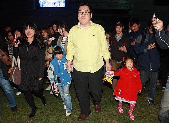 인터넷 시사라디오 '나는 꼼수다'의 김용민 평론가가 26일 저녁 서울시청광장에서 시민으로부터 선물받은 꼬깔콘을 아이에게 건네주고 함께 손을 잡고 사인회장으로 이동하고 있다.