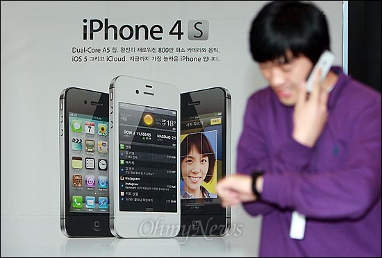 아이폰4S가 KT와 SK텔레콤을 통해 동시 출시된 11월 11일 오전 서울 광화문 KT사옥 올레스퀘어에서 한 시민이 휴대전화 통화하며 아이폰4S 출시를 알리는 광고판 앞을 지나가고 있다.
