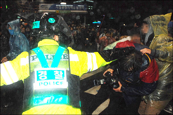 11월 23일 밤 서울광장 인근에서 '한미FTA 국회비준 무효' 시위가 벌어진 가운데, 시위대 검거작전을 펼치던 경찰관 한 명이 사진기자의 머리채를 잡은 채 강제연행을 시도하고 있다.