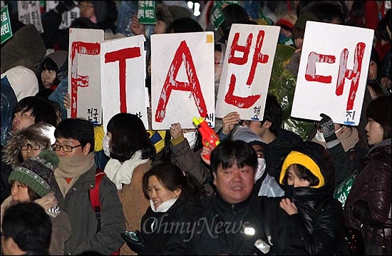 24일 저녁 서울시청광장에서 열린 '한미FTA 날치기 무효, 이명박 퇴진, 한나라당 해체 촛불집회'를 마친 참가자들이 'FTA반대'라고 적힌 피켓을 들어보이며 거리행진을 하고 있다.