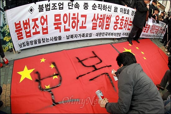 어버이연합 회원들과 함께 규탄집회에 참석한 한 탈북자가 '오성홍기'에 '보복' '응징'을 쓰고 있다.