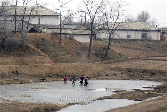 꽁꽁 얼어붙은 동네 논 바닥에서 어린이들이 썰매를 타고 있다.