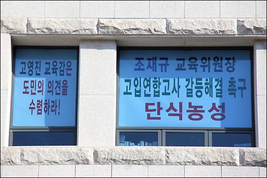  경상남도교육청이 고입 연합고사를 부활하겠다고 해 논란을 빚고 있는 속에, 경상남도의회 조재규 교육위원장은 사무실 유리창에 '찬반 공동설문조사' 실시를 요구하는 펼침막을 붙여 놓았다.