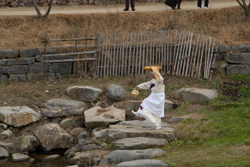 술안주 이고 술주전자를 들고 신바람나게 징검다리를 건너는 주모. 2010년 3월 6일 아산외암리민속마을에서 