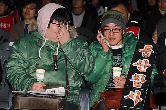 19일 오후 서울 중구 서울역 광장에서 열린 '용산참사 3주기 추모대회'에서 학생들이 추모영상을 지켜보며 손으로 눈물을 훔치고 있다.