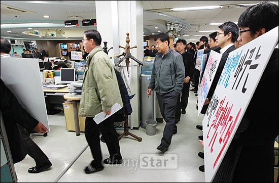 26기 이하 MBC 기자들의 제작거부 첫날인 25일 오전 서울 여의도 MBC본사 5층 보도국에서 기자들이 침묵시위를 하고 있는 사이로 각 부장들이 아침편집회의를 위해 회의실로 가고 있다.