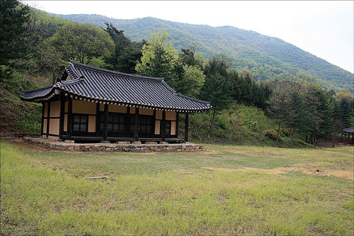 김유신 생가. 뒤로 김유신의 태실이 정상에 묻혀 있는 태령산이 보인다. 사진 오른쪽 끝에 유허비도 조그맣게 보인다.