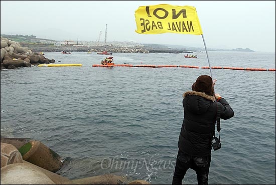 해군이 구럼비 바위 지역의 발파를 시작한 7일 오전 제주도 서귀포시 강정포구에서 한 시민이 해군기지 건설 중단을 요구하며 깃발을 흔들어 보이고 있다.