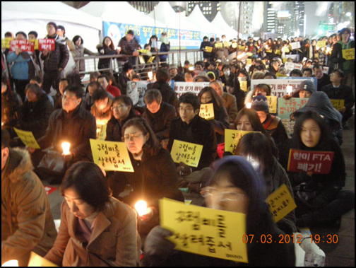 시민들이 '구럼비를 살려줍서"라는 피켓과 촛불을 들고 앉아 있다.