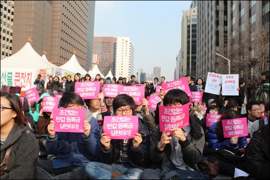 대학생들이 '반값등록금 실현하라'는 플래카드를 들고 응원하고 있다. 지나가던 시민들도 삭발식을 지켜보고 있다