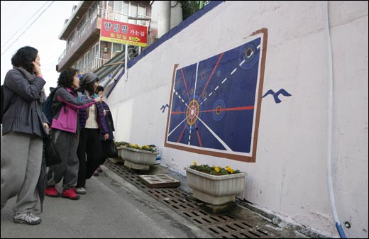 향일암에서 내려오는 여행객들이 박진용 화백이 그리고 있는 벽화를 보고 있다.